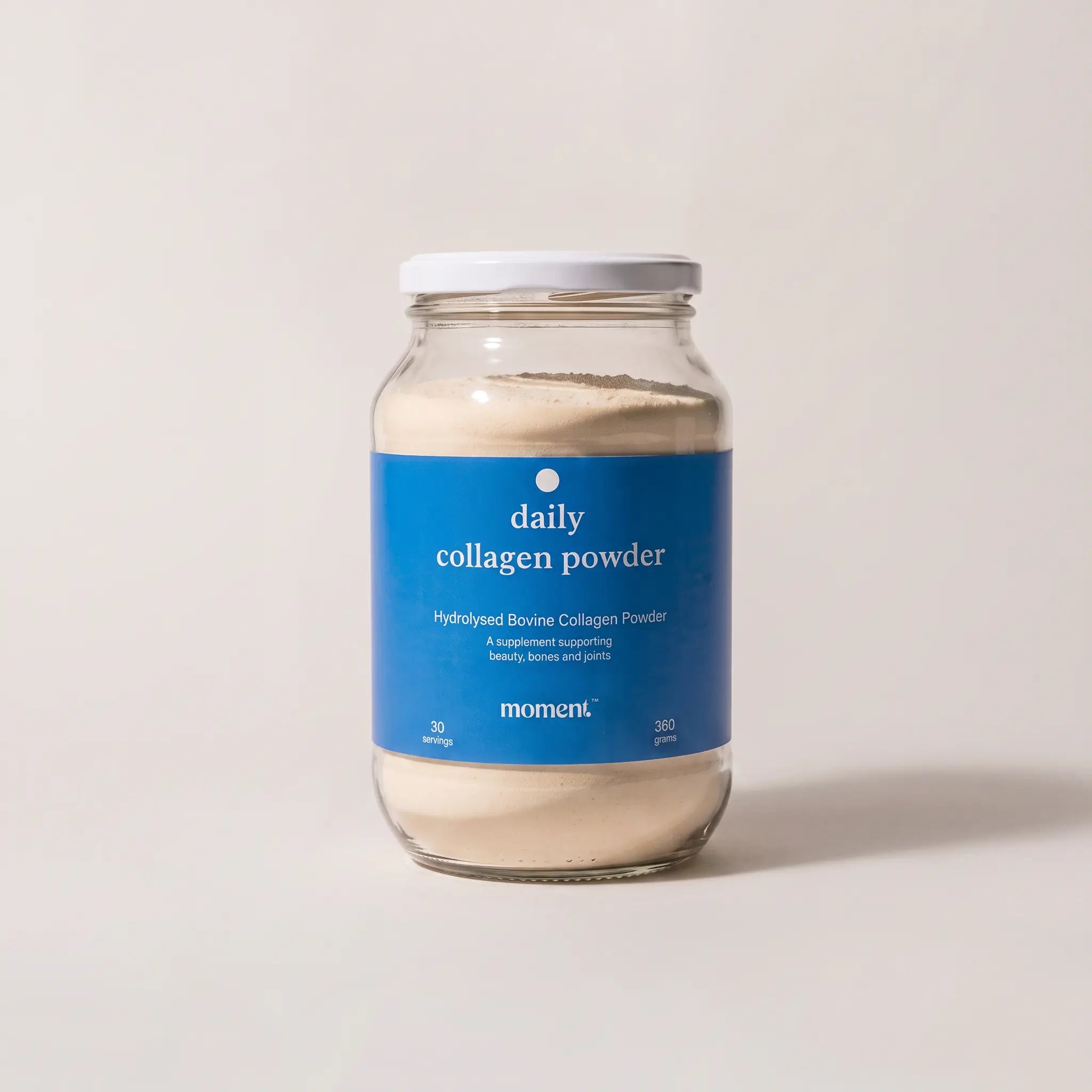 A glass jar of Moment Hydrolysed Bovine Collagen Powder with a blue label and white lid, set against a plain light beige background.