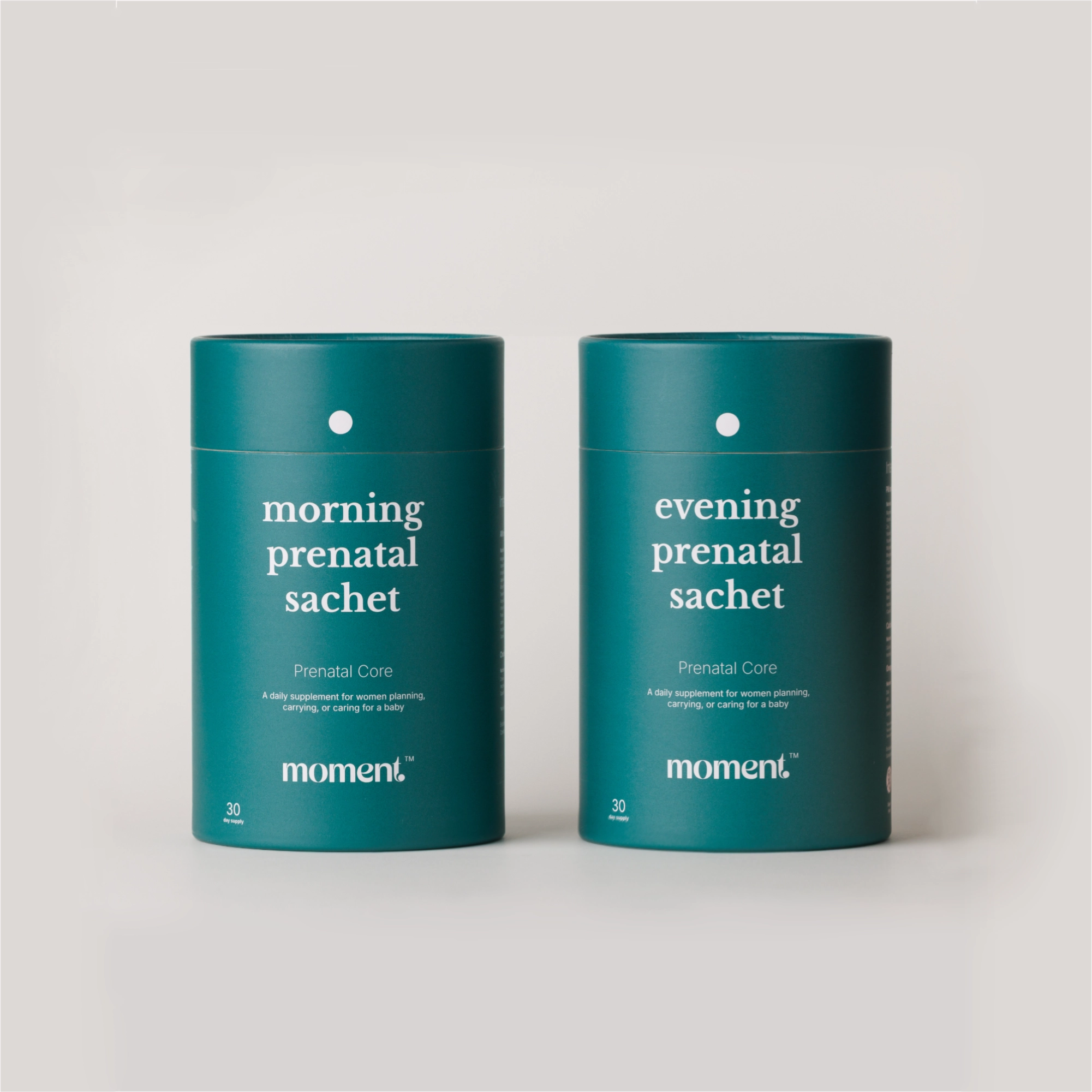 Two teal cylindrical supplement tins labeled 'morning prenatal sachet' and 'evening prenatal sachet' by moment, shown on a light gray background.